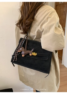 Detail view of black suede satchel with golden clasp and brown dachshund charm detail