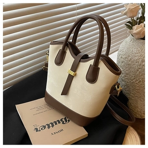 Détail d'un sac seau bicolore avec finitions en cuir marron et boucle en métal doré