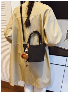 Dettaglio borsa a secchiello nera con ciondolo in peluche su modella in trench kaki