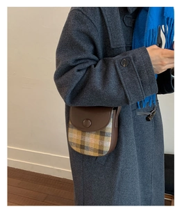 Close-up of vintage plaid saddle bag with brown leather flap on a grey wool coat