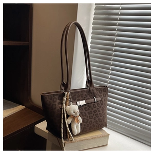 Detail of dark brown leopard print tote bag with plush bear and woven tassel charms