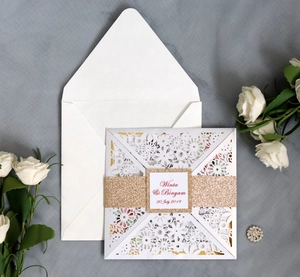 Macro shot of laser-cut floral wedding invitation with gold glitter band and white envelope
