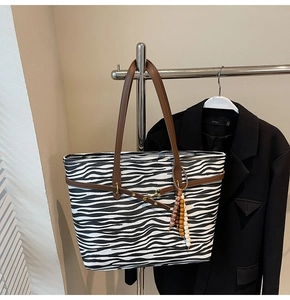 Detail of zebra print tote bag featuring brown leather straps and beaded tassel charm