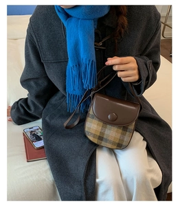 Detail of vintage saddle bag with brown leather and plaid fabric on model's gray coat