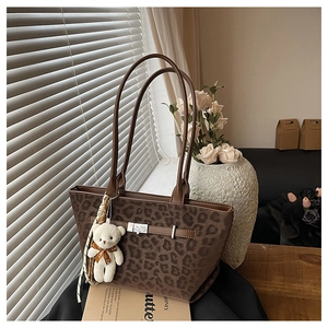 Detail of leopard print tote bag featuring brown leather straps and cute bear charm