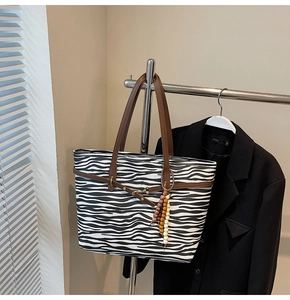Zebra pattern tote bag detail with brown leather handles and decorative beaded tassel charm