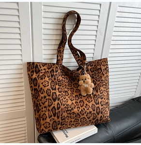 Leopard print velvet tote bag with a brown plush bear charm shown in a minimalist setting