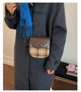 Detail of a vintage plaid crossbody saddle bag with brown leather flap and decorative buckle