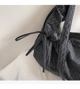 Detail of checkered canvas shoulder bag with drawstring closure and decorative bow detail