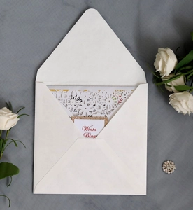 Macro detail of laser-cut lace floral pattern on ivory wedding invitation with gold trim