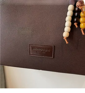 Gros plan du sac fourre-tout marron foncé avec étiquette de marque et perles en bois