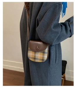 Detail of checkered tweed saddle bag with dark brown leather strap worn over a grey coat