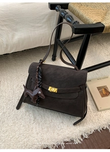 Detail of dark brown suede handbag featuring golden twist lock and leather puppy charm