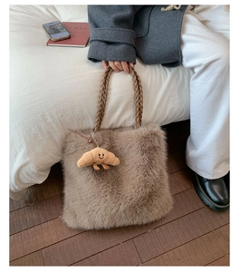 Detail of soft brown plush tote bag featuring a cute croissant charm and woven handles