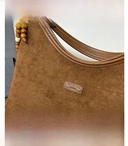 Detail of coffee brown suede shoulder bag with leather handle and wooden bead charm