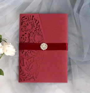Detail of burgundy laser-cut floral invitation with silk ribbon and rhinestone buckle