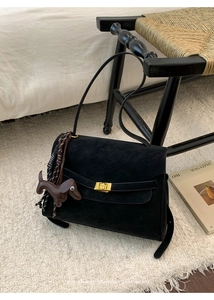 Detail of black suede shoulder bag with golden buckle and brown dog charm accessory