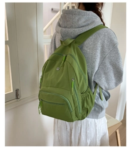 Seitenansicht eines grünen Nylon-Rucksacks mit mehreren Taschen, von einem Modell getragen