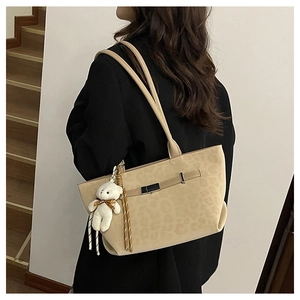 Close-up of beige suede tote bag with leopard pattern, metal buckle, and bear charm