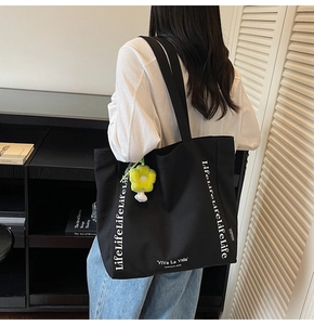 Detail of black canvas tote bag featuring white graphic text and sunflower plush charm