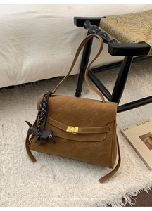 Brown retro commuter bag with golden buckle and dog charm on a woven chair