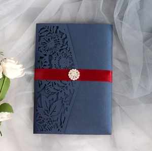 Detail of dark blue laser-cut invitation with red satin ribbon and rhinestone flower brooch