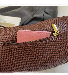 Detail of dark brown woven shoulder bag with golden zipper pocket holding a wallet