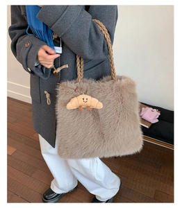 Detail of light brown plush tote bag featuring braided handles and a croissant charm