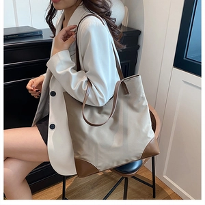 Close-up of a large minimalist tote bag with leather trim held by a model in a white suit