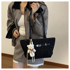 Detail of black leopard texture tote bag with silver lock and white bear plush charm