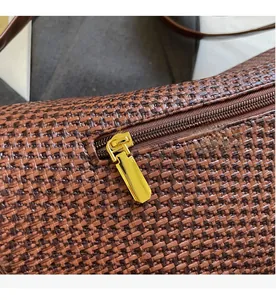 Detailed close-up of smooth gold metal zipper on brown woven leather crossbody bag