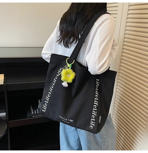 Detail of black canvas tote bag with white Life letters and sunflower charm on a model