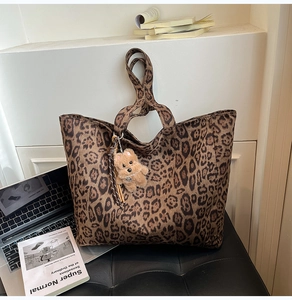 Detail of leopard print tote bag with plush dog charm and leather tassel on a black chair