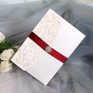 Macro shot of white laser-cut floral invitation with burgundy ribbon and crystal buckle