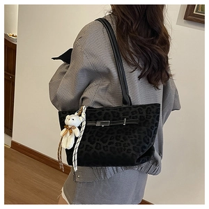 Detail of black leopard print tote bag with white plush bear charm on a female model