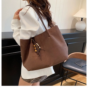 Brown suede tote bag side view with wooden beads and leather fringe charm on a model