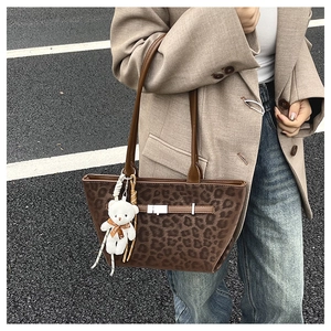 Detail of leopard print tote bag with brown leather handles and a plush white bear charm