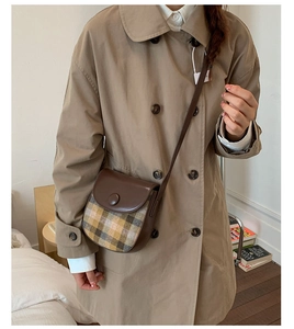 Detail of vintage saddle bag with brown leather and grey plaid fabric on a trench coat