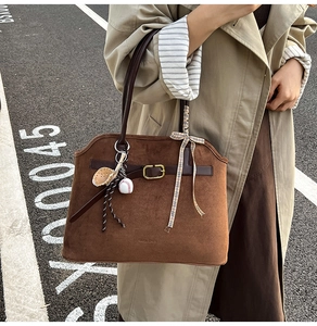 Detail of suede tote bag featuring leather straps, metal buckle, and baseball charm