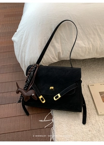 Detail of a minimalist black matte leather tote with gold buckles and a cute dog charm