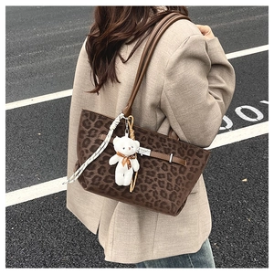 Detail of leopard print tote bag featuring leather strap buckle and plush bear pendant