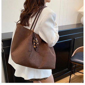 Detail of caramel brown tote bag with vintage wooden bead charm and suede texture