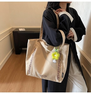 Detail of beige canvas tote bag featuring printed text and a yellow flower charm