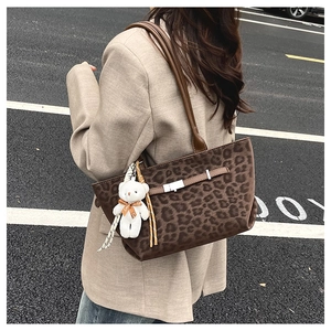 Detail of leopard print tote bag featuring a leather strap and plush bear charm