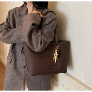 Détail d'un grand sac cabas en cuir marron foncé avec pendentif perlé porté à l'épaule