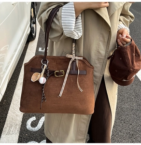 Detail of a brown suede tote bag with metal lock buckle and baseball charm accessory