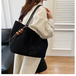 Detail of black tote bag with retro wooden bead pendant worn over a white coat