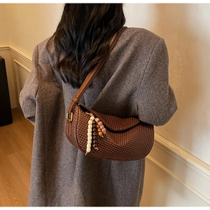 Detail of a brown woven hobo bag with ethnic bead charm on a grey plaid blazer