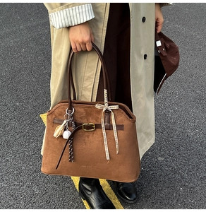 Detail of vintage brown suede tote bag with ribbon bow and creative charms on leather handle
