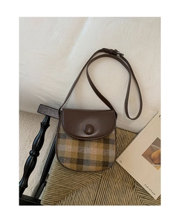 Close-up of vintage plaid saddle bag with brown leather flap on a woven chair